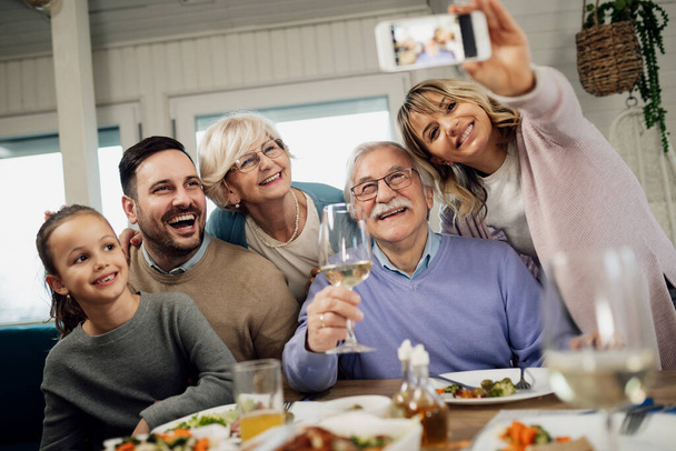 Low angle view of happy extended family having fun while taking selfie after lunch at dining table.  - Fotografie, Obrázek