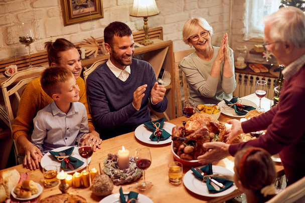Щаслива розширена сім'я, насолоджуючись обідом на День Подяки в їдальні. Старший чоловік подає смажену індичку
. - Фото, зображення