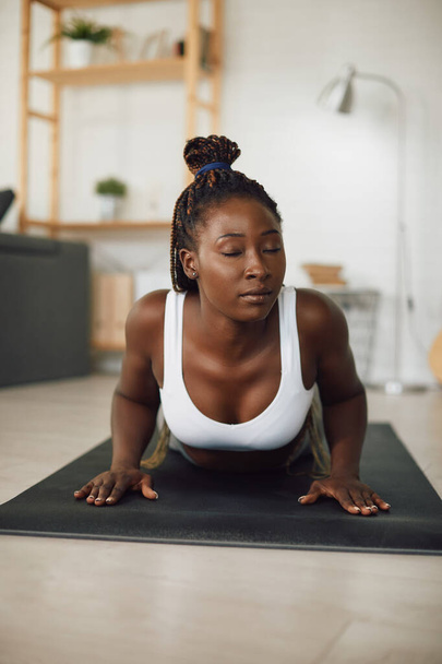 Young black sportswoman practicing Yoga relaxation exercises while working out at home. - Foto, Imagen