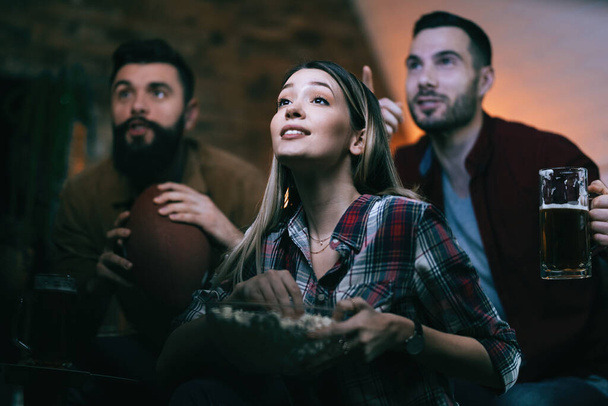 Low angle view of sport fans watching game on TV at home. Focus is on woman with popcorn.  - Foto, imagen