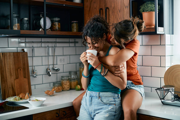 Young happy lesbian women drinking coffee and having fun in the kitchen. - Фото, зображення