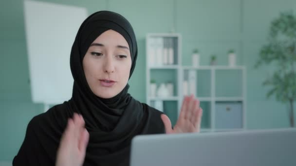 Mówiąca muzułmańska islamska kobieta komunikująca się przez połączenie wideo wyjaśnia. Ethnic Arabian remote teacher in hijab speaking looking at laptop komputer ekran lekcja konferencja odległość biuro czat wirtualny - Materiał filmowy, wideo