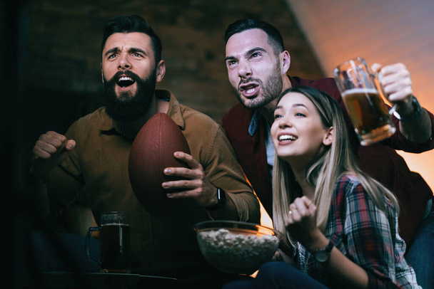 Group of excited friends cheering for their team while watching sport championship on TV at home.  - 写真・画像