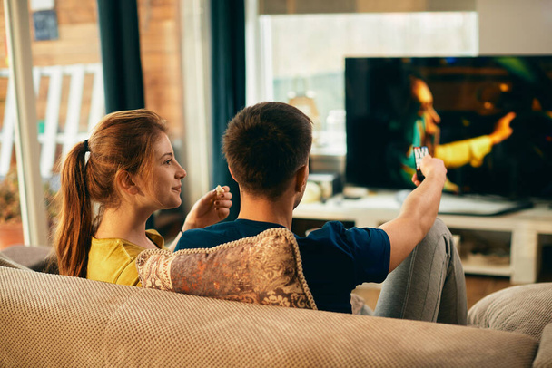 Молода жінка їсть попкорн і дивиться фільм по телевізору зі своїм хлопцем вдома
.  - Фото, зображення