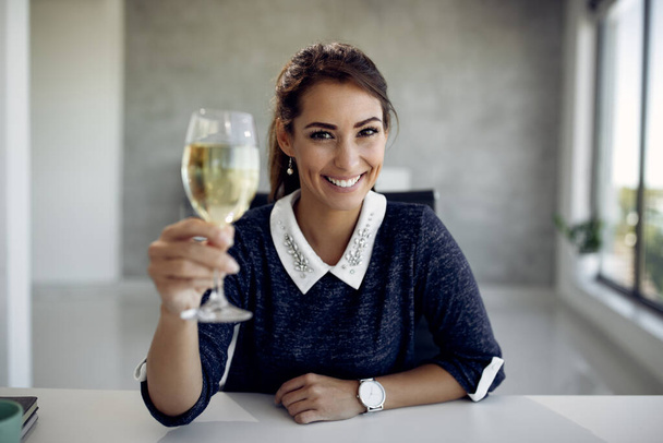 Happy businesswoman toasting with wineglass during video call and looking at camera.  - Photo, Image