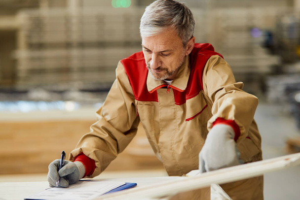 Ξυλουργός ελέγχει τις μετρήσεις ενώ εργάζεται σε ένα νέο έργο στο εργαστήριο ξυλουργικής.  - Φωτογραφία, εικόνα