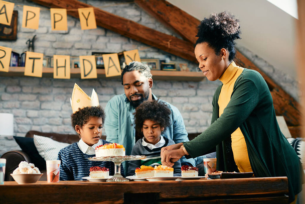 Glückliche afroamerikanische Mutter serviert Kuchen während der Geburtstagsparty ihres Sohnes zu Hause. - Foto, Bild