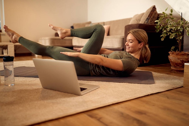 Щаслива жінка-спортсменка використовує ноутбук під час тренувань на підлозі у вітальні
.  - Фото, зображення