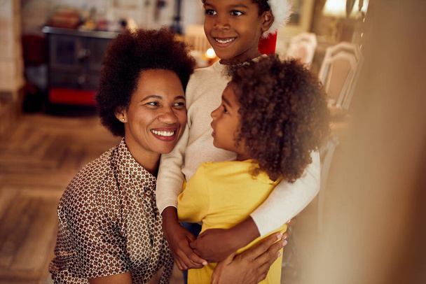 Happy black mother embracing her kids while spending Christmas together at home.  - Foto, Bild