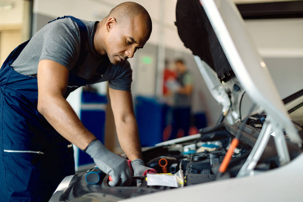 Black auto repairman using wrench while working on car engine in a workshop.  - Foto, Bild