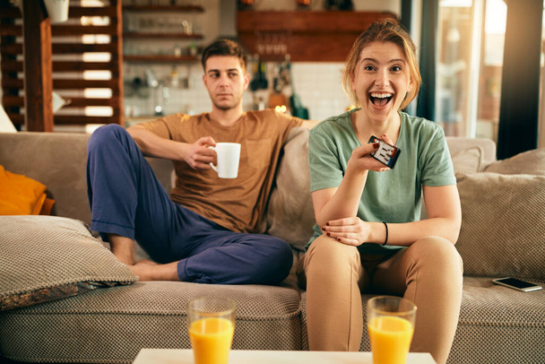 Happy woman having fun while changing channels and watching Tv with her boyfriend at home.  - Foto, Imagen