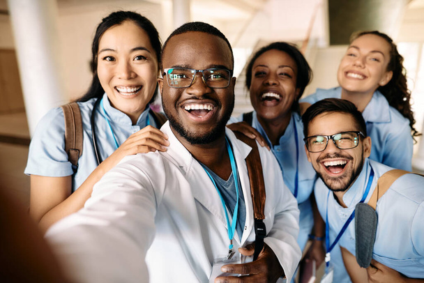 Πολυεθνική ομάδα χαρούμενων φοιτητών που διασκεδάζουν βγάζοντας selfie στο ιατρικό πανεπιστήμιο. - Φωτογραφία, εικόνα