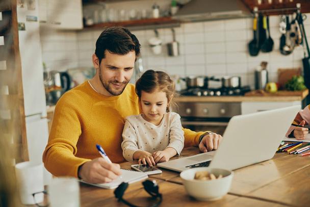 Smiling father working at home while daughter is sitting on his lap. - 写真・画像