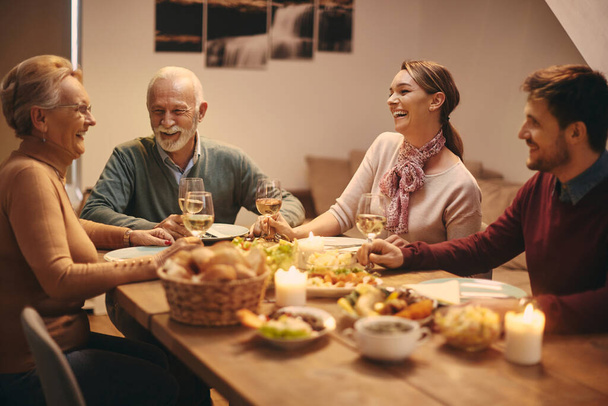 Щаслива старша пара та їхні дорослі діти розважаються під час пиття вина та спілкування за обіднім столом
.  - Фото, зображення