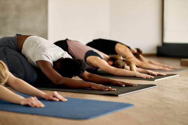 Group of female athletes warming up and stretching on the floor during Yoga class at health club. Focus is on black woman. - Foto, imagen