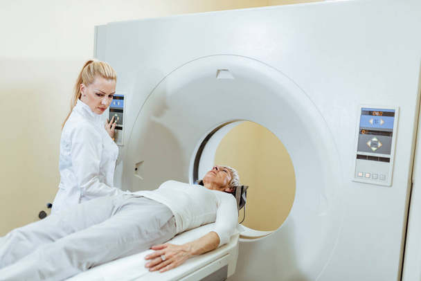 Vrouwelijke medische technicus en volwassen patiënt tijdens CT-scan procedure in onderzoekskamer in het ziekenhuis.  - Foto, afbeelding