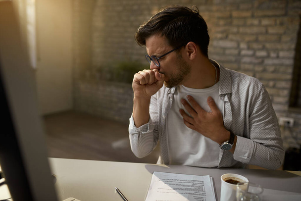 Sick entrepreneur coughing while working at his office desk.  - Photo, image