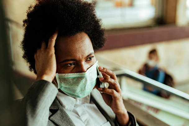 Distraught African American businesswoman with protective face mask making a phone call while being at airport corridor.  - Photo, Image