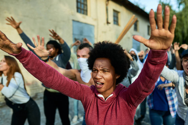 Black woman with raised arms shouting while participating in public demonstrations on the streets.  - Foto, Imagem
