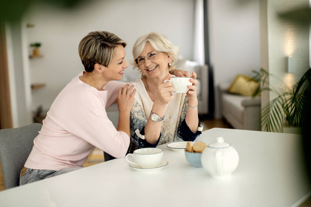 Счастливая женщина и ее зрелая мать наслаждаются чашечкой кофе дома.  - Фото, изображение