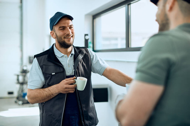 Young auto repair man drinking coffee and communicating with a colleague in a workshop. - 写真・画像