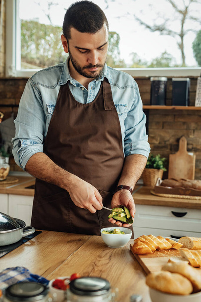 Mladý muž peeling avokádo při přípravě jídla v kuchyni.  - Fotografie, Obrázek