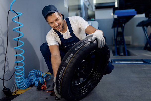 Happy mechanic working with car tire at auto repair shop. - Φωτογραφία, εικόνα