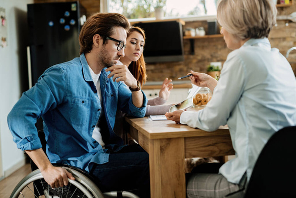 Young couple using touchpad with their insurance agent while having a meeting at home. Focus is on man in wheelchair.  - Photo, Image