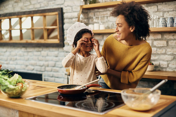 Playful black little girl and her mother having fun with food while making a meal in the kitchen. - Foto, imagen