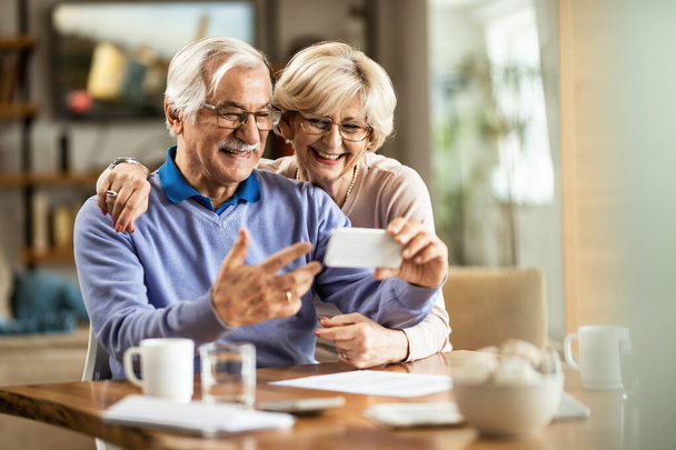Glückliches Senioren-Paar hat Spaß beim Videoanruf über Handy zu Hause.  - Foto, Bild
