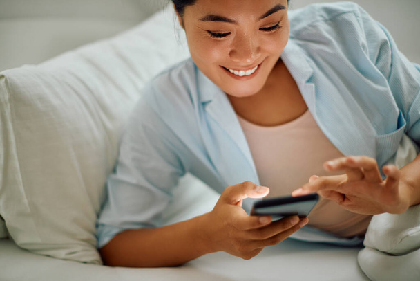 Happy Asian woman using smart phone while relaxing on a bed at home. - Foto, immagini