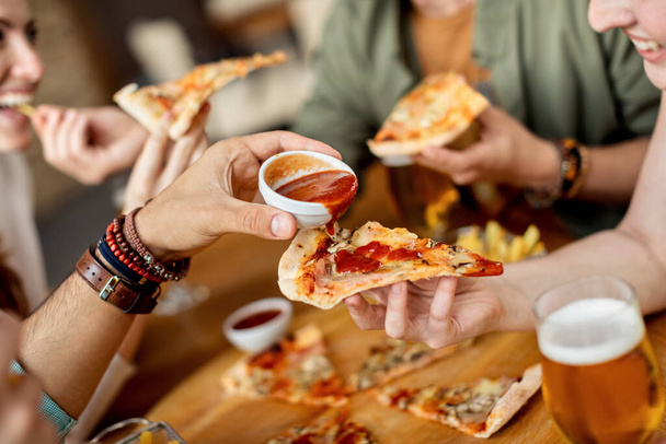 Close-up of man pouring ketchup on friend's slice of pizza.  - 写真・画像