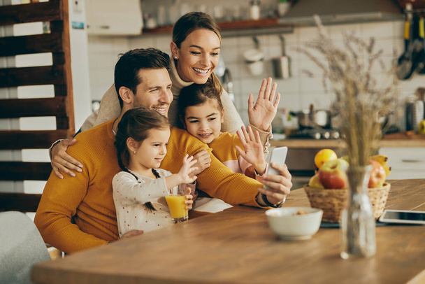 Happy parents with daughters greeting someone during video chat over mobile phone at home. - Φωτογραφία, εικόνα