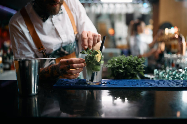 Close-up of barista using herbs while making mojito cocktail in a pub. - Foto, Imagen