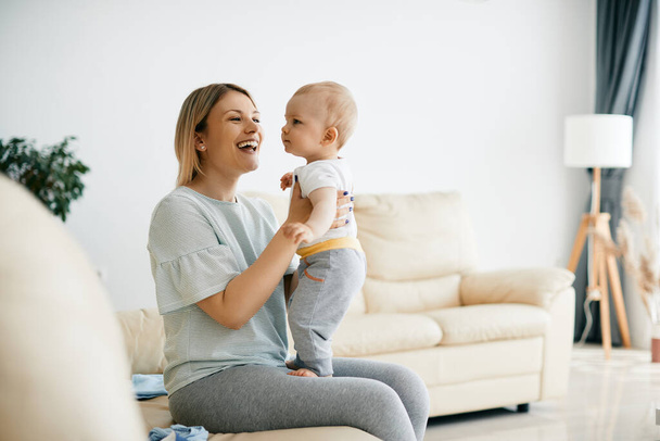 Young cheerful mother having fun with her baby boy at home.  - Photo, Image