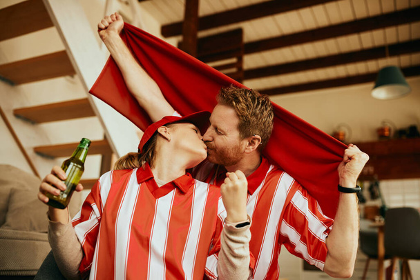 Excited couple in sports uniform kissing while watching game and celebrating winning of their favorite team. - 写真・画像