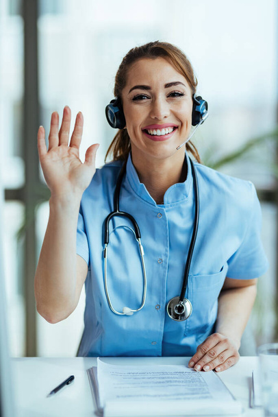 Happy healthcare worker waving while working at medical call center.  - Foto, imagen