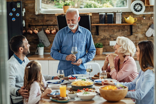 Щасливий старший чоловік тримає тост, обідаючи зі своєю родиною за обіднім столом
.  - Фото, зображення