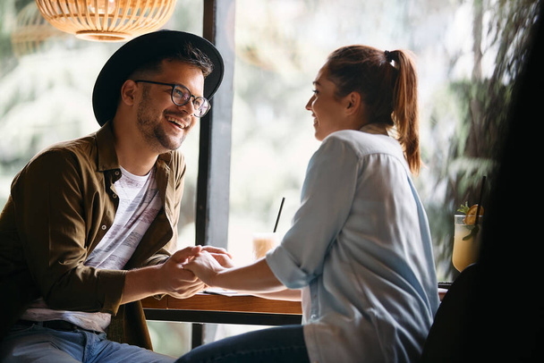Молодий щасливий чоловік і його дівчина спілкуються, тримаючись за руки і сидячи в кафе
.  - Фото, зображення