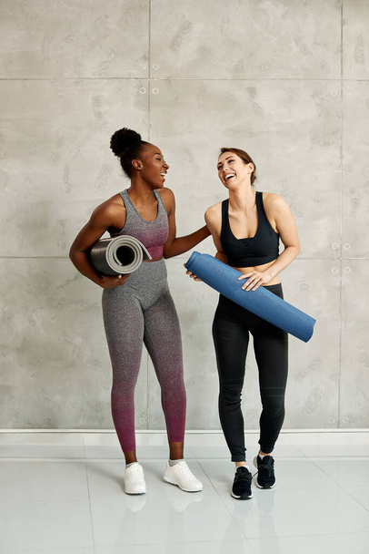 Happy African American sportswoman and her Caucasian female friend having fun and laughing against the wall at health club. Copy space.  - Photo, Image