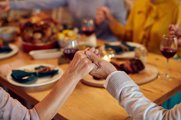 Close-up of grateful family holding hands and praying before Thanksgiving dinner at dining table.  - Foto, afbeelding