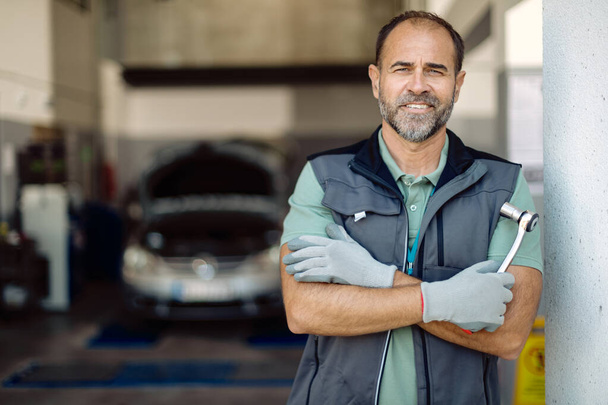 Portrait of happy auto mechanic standing with crossed arms at repair shop and looking at camera.  - Foto, imagen