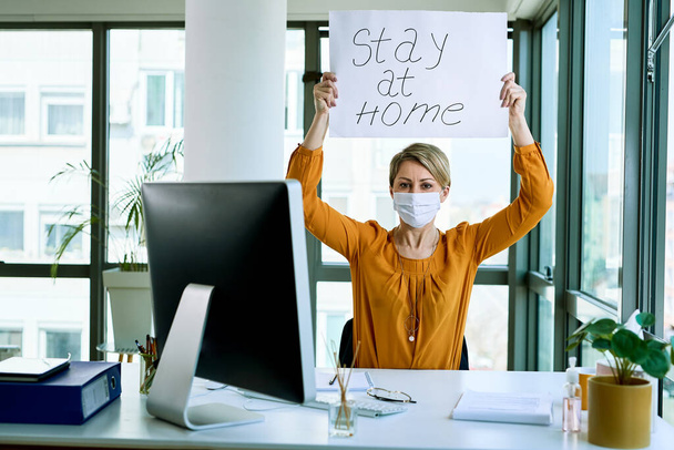 Businesswoman holding placard with stay at home text as appeal during virus epidemic.  - 写真・画像