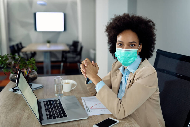 Afro-Amerikaanse zakenvrouw werkt op een computer en haar bureau en draagt gezichtsmasker als gevolg van COVID-19 pandemie.  - Foto, afbeelding
