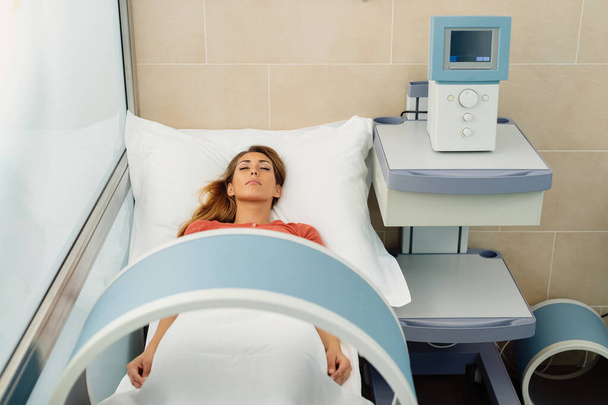 Молода жінка лежить з закритими очима під час магнітотерапії в оздоровчому спа-центрі
.  - Фото, зображення