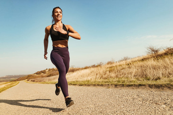 Low angle view of young happy athletic woman running on the road.  - Foto, imagen