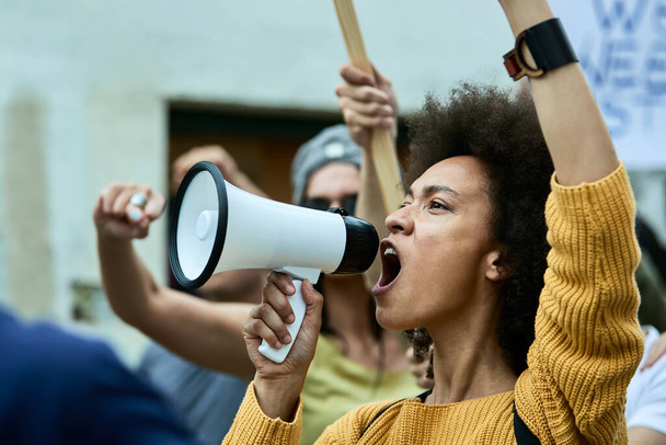 Young black woman shouting through megaphone on public demonstrations against racism.  - 写真・画像
