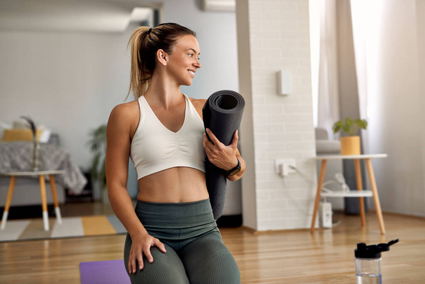 Happy athletic woman holing exercise mat while preparing for workout at home.  - Photo, Image