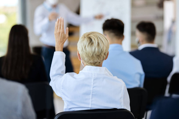 πίσω όψη μιας επιχειρηματία που παρακολουθεί ένα σεμινάριο και σηκώνει το χέρι της για να κάνει μια ερώτηση.  - Φωτογραφία, εικόνα