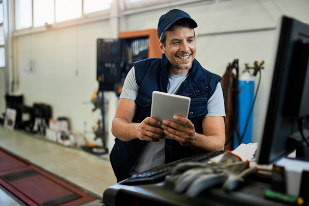 Happy auto repairman using desktop PC and digital tablet while working in a workshop.  - Foto, Bild